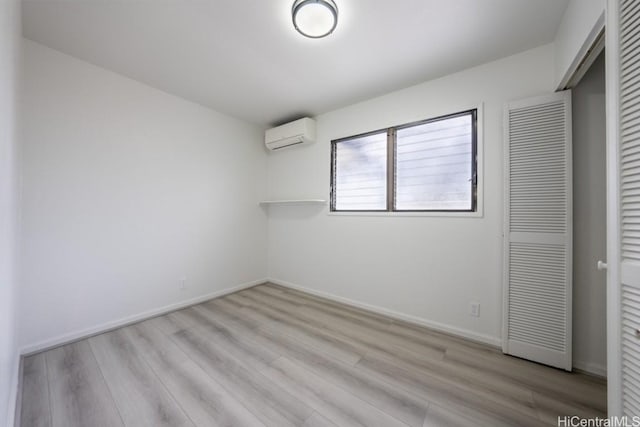 unfurnished bedroom with a wall mounted air conditioner, light hardwood / wood-style flooring, and a closet