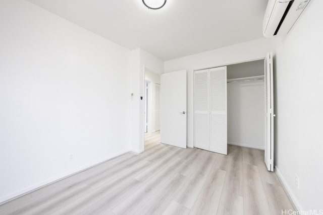 unfurnished bedroom with a wall mounted air conditioner, a closet, and light wood-type flooring