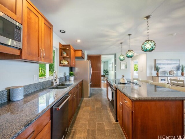 kitchen with sink, appliances with stainless steel finishes, a kitchen island, pendant lighting, and dark stone counters