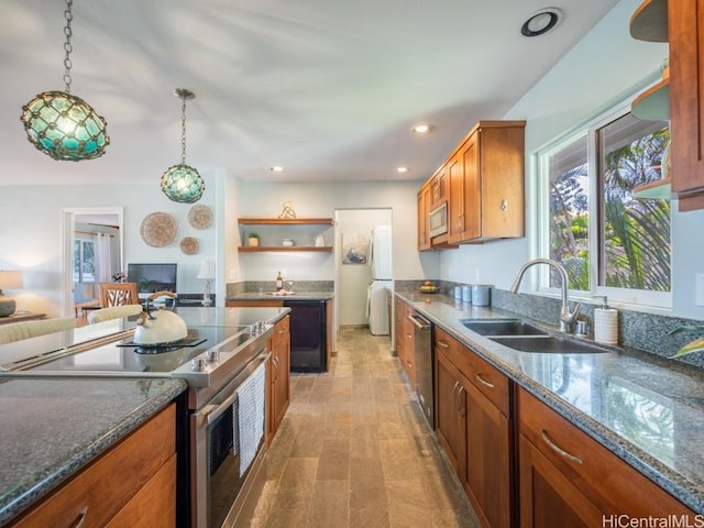 kitchen with decorative light fixtures, sink, dark stone countertops, light hardwood / wood-style floors, and stainless steel appliances