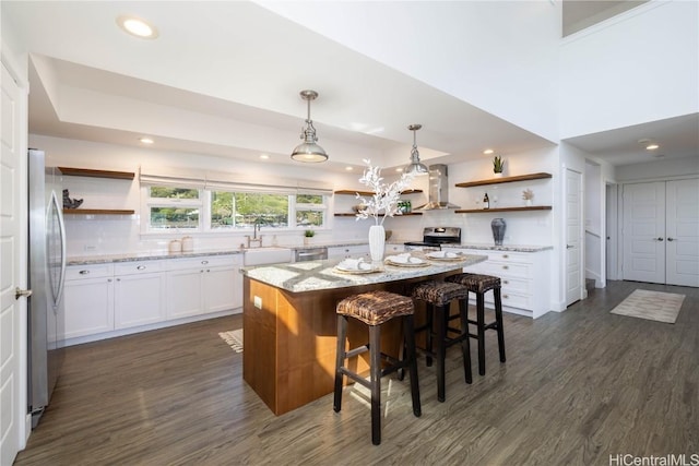 kitchen with wall chimney range hood, a breakfast bar, appliances with stainless steel finishes, white cabinetry, and a kitchen island