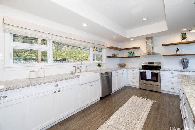 kitchen with appliances with stainless steel finishes, sink, wall chimney range hood, and white cabinets