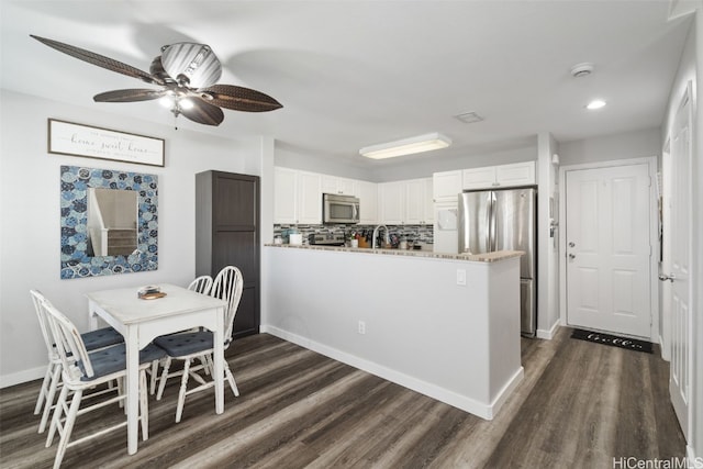 kitchen with dark wood-type flooring, appliances with stainless steel finishes, white cabinetry, decorative backsplash, and kitchen peninsula