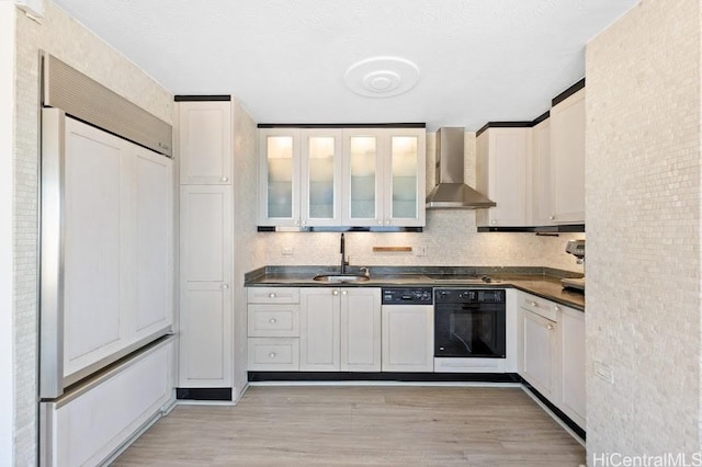 kitchen featuring sink, paneled appliances, white cabinets, light hardwood / wood-style floors, and wall chimney range hood