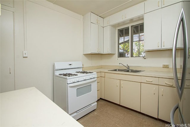 kitchen featuring sink, white cabinetry, white gas range, and stainless steel refrigerator