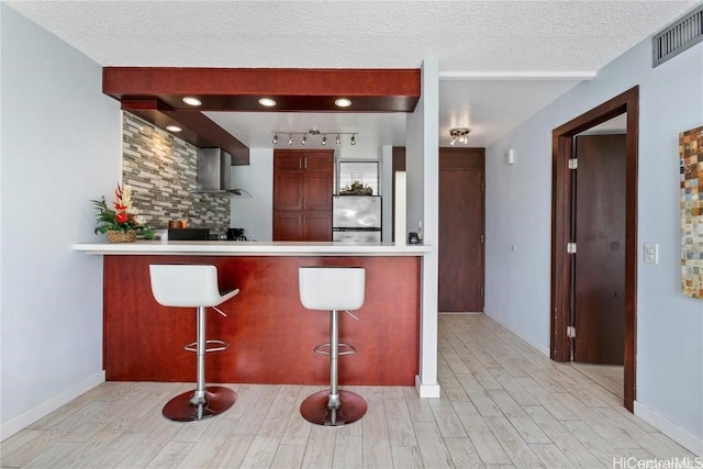 kitchen with a textured ceiling, kitchen peninsula, stainless steel refrigerator, light hardwood / wood-style flooring, and a breakfast bar area