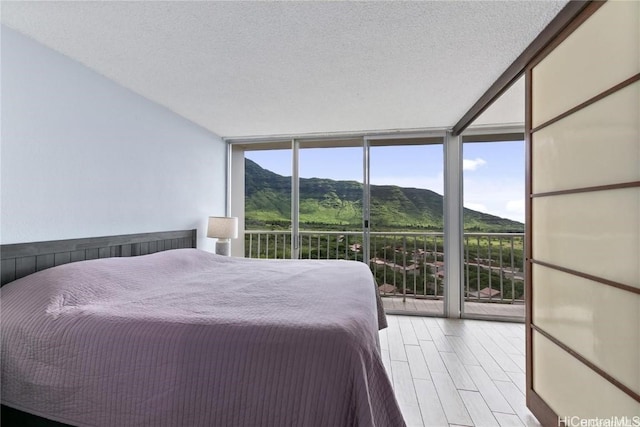 bedroom with a mountain view, a textured ceiling, a wall of windows, and light wood-type flooring