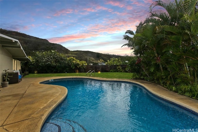 pool at dusk featuring a mountain view, a patio area, and a lawn