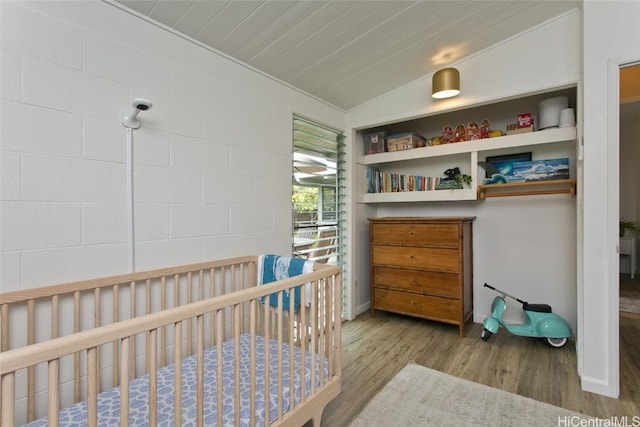 bedroom featuring light wood-type flooring, vaulted ceiling, and a nursery area