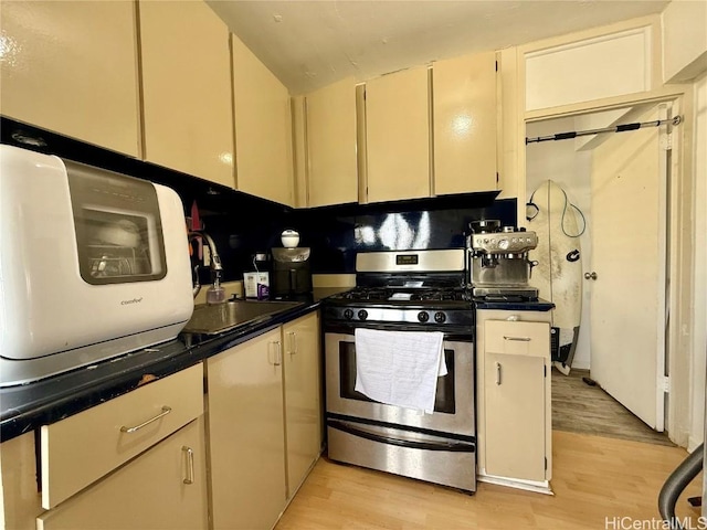 kitchen with sink, light wood-type flooring, stainless steel range with gas cooktop, and cream cabinetry