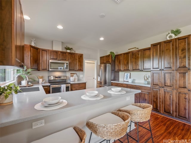 kitchen with appliances with stainless steel finishes, a kitchen breakfast bar, sink, dark hardwood / wood-style floors, and kitchen peninsula