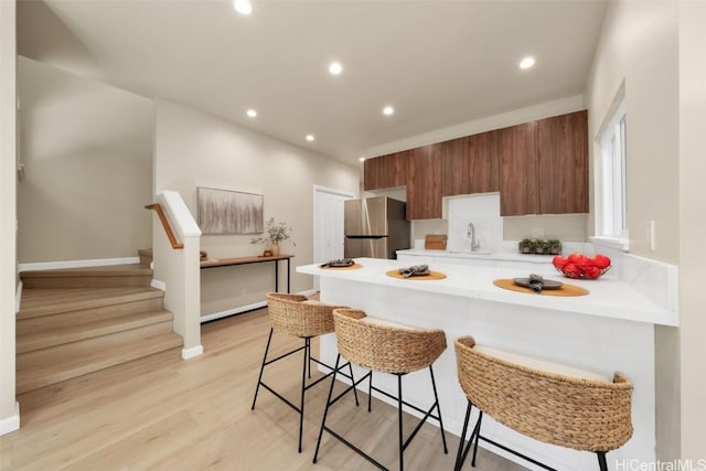 kitchen featuring kitchen peninsula, a breakfast bar area, stainless steel refrigerator, light hardwood / wood-style flooring, and sink