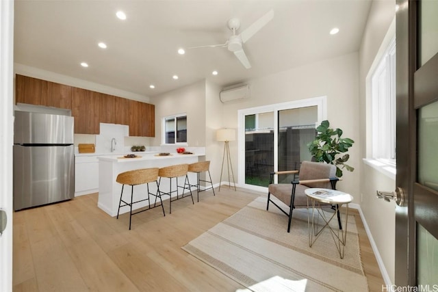 kitchen with light hardwood / wood-style floors, stainless steel fridge, kitchen peninsula, a wall mounted AC, and a breakfast bar area