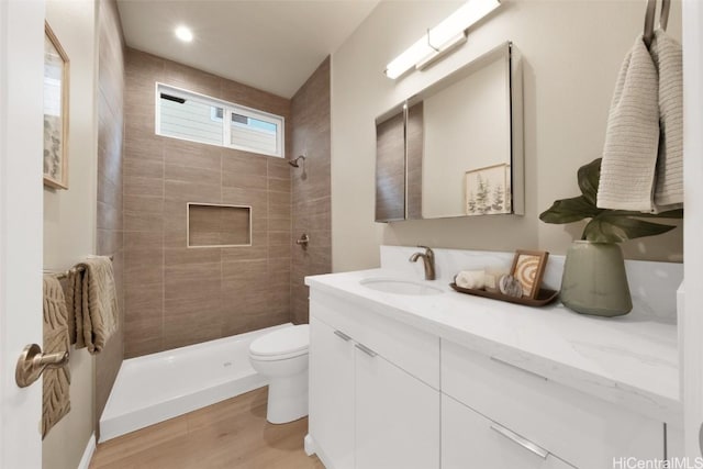 bathroom featuring hardwood / wood-style floors, tiled shower, vanity, and toilet