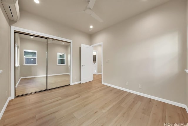 unfurnished bedroom with ceiling fan, a closet, light hardwood / wood-style floors, and a wall unit AC