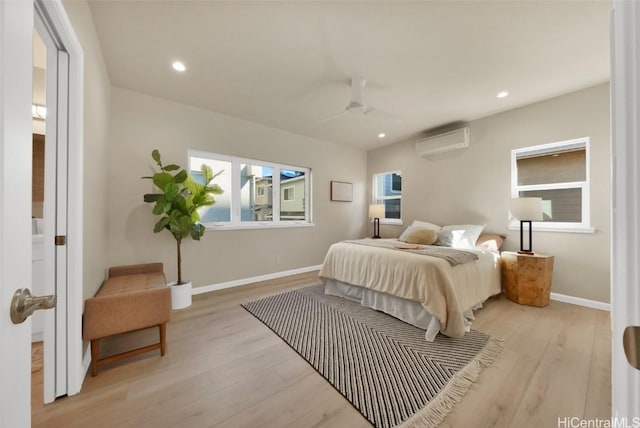 bedroom with ceiling fan, a wall mounted AC, and light hardwood / wood-style flooring