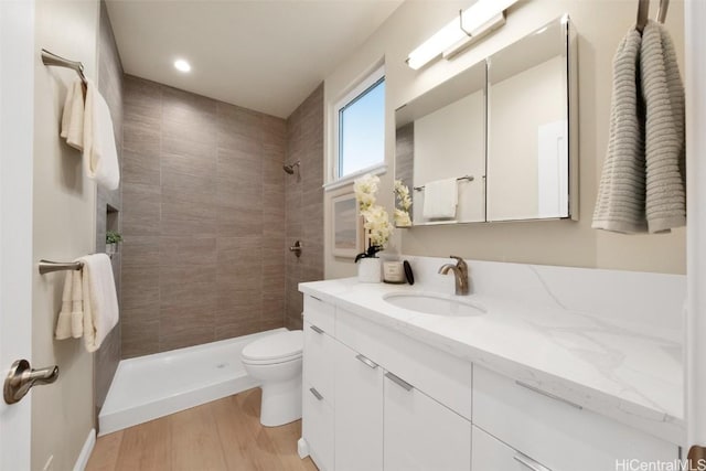 bathroom featuring toilet, vanity, a tile shower, and hardwood / wood-style flooring