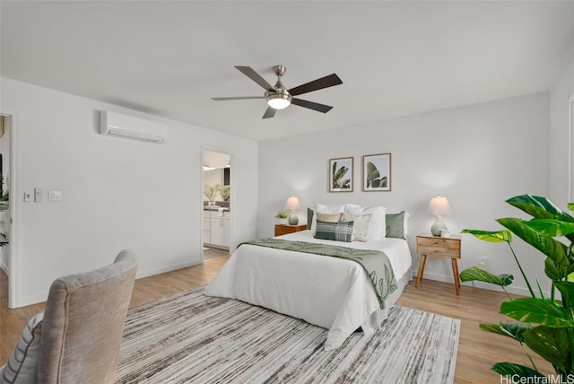 bedroom featuring ceiling fan, ensuite bathroom, a wall unit AC, and light wood-type flooring