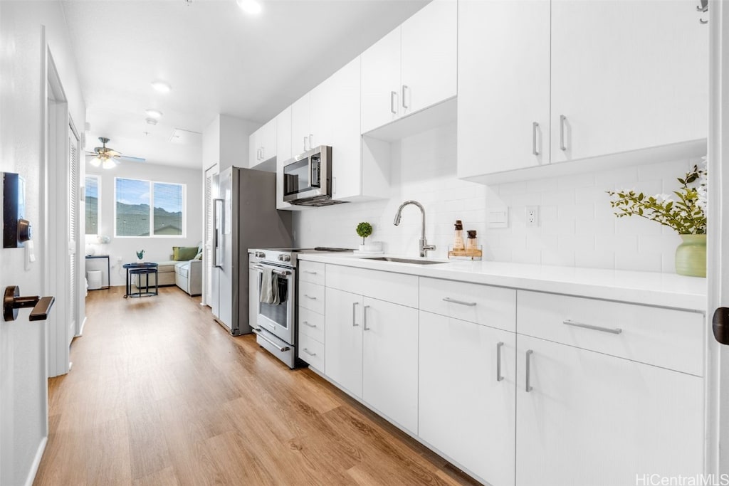 kitchen featuring white cabinetry, sink, light wood-type flooring, backsplash, and stainless steel appliances