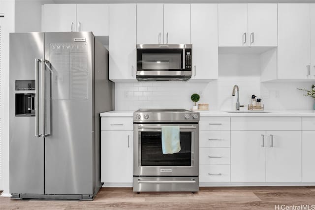 kitchen featuring hardwood / wood-style floors, white cabinets, stainless steel appliances, tasteful backsplash, and sink