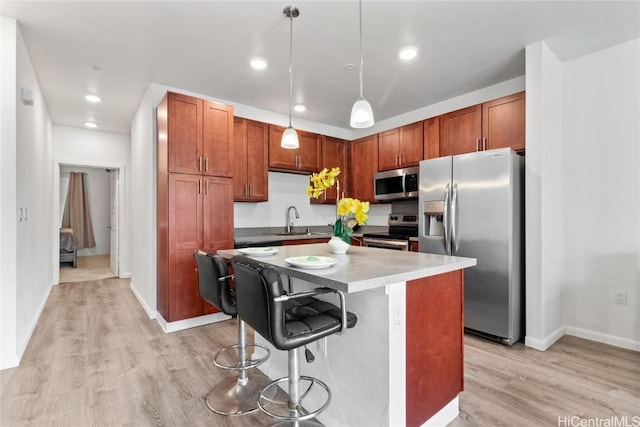 kitchen featuring sink, appliances with stainless steel finishes, a kitchen breakfast bar, a kitchen island, and decorative light fixtures