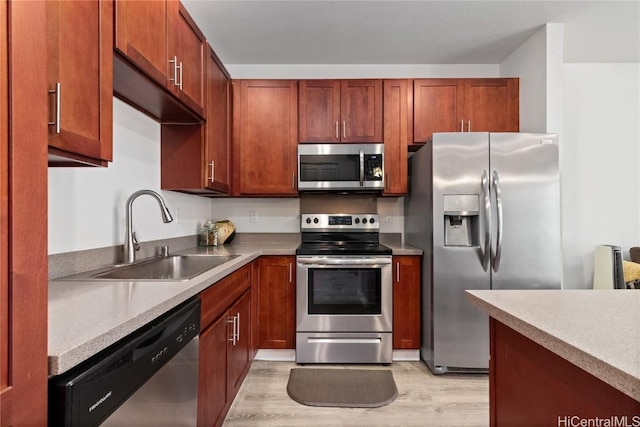 kitchen with appliances with stainless steel finishes, sink, and light wood-type flooring