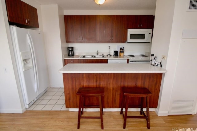 kitchen featuring white appliances, sink, kitchen peninsula, light tile patterned flooring, and a breakfast bar area