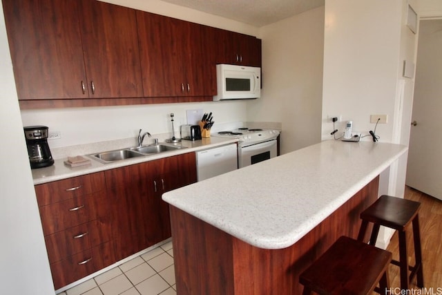 kitchen with a breakfast bar, kitchen peninsula, sink, white appliances, and light tile patterned flooring