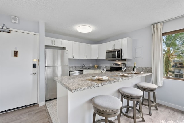 kitchen featuring light wood-type flooring, a kitchen breakfast bar, kitchen peninsula, stainless steel appliances, and white cabinets