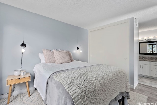 bedroom featuring ensuite bath, light hardwood / wood-style floors, and a textured ceiling