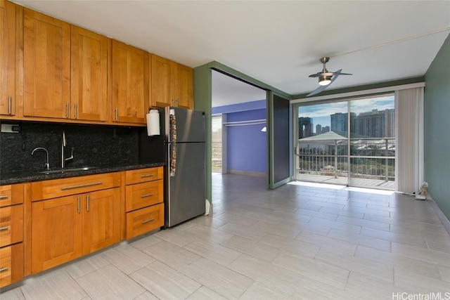 kitchen featuring ceiling fan, backsplash, dark stone countertops, sink, and stainless steel fridge