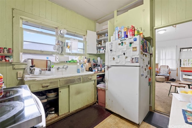 kitchen with green cabinets, white fridge, and wood walls