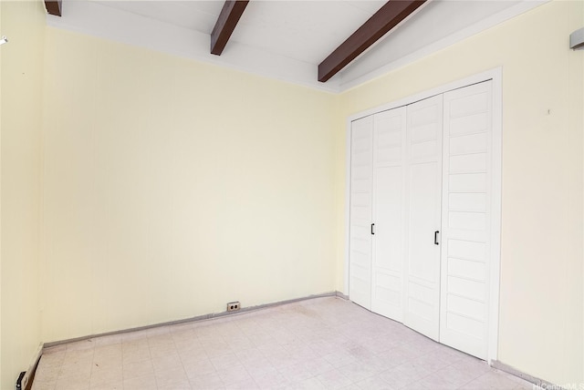 unfurnished bedroom featuring beamed ceiling, light floors, and a closet