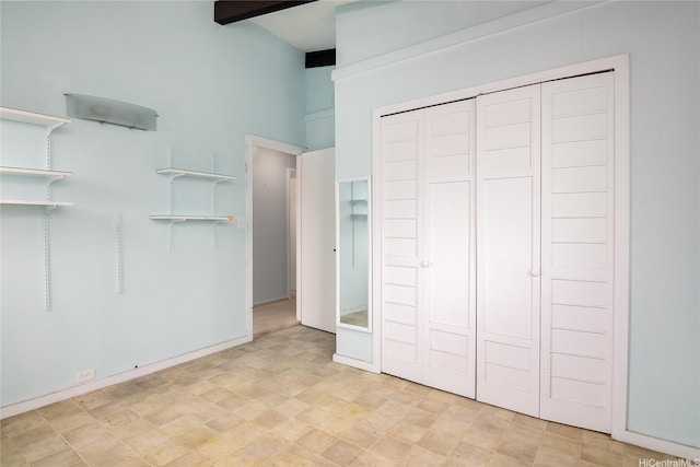 unfurnished bedroom featuring a high ceiling, a closet, and beam ceiling