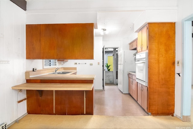 kitchen with a sink, white appliances, light countertops, brown cabinetry, and a peninsula