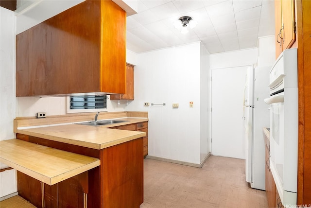 kitchen with white oven, brown cabinets, a sink, light countertops, and a peninsula