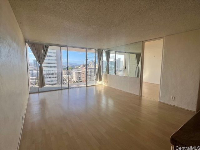 empty room featuring a textured ceiling, a wall of windows, and light hardwood / wood-style flooring