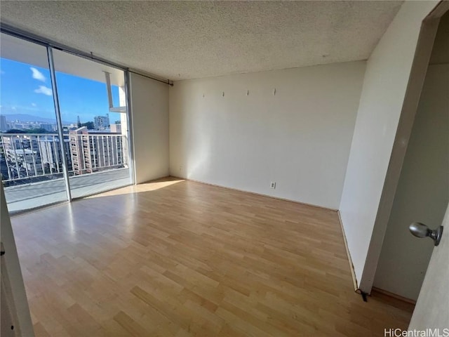 unfurnished room featuring floor to ceiling windows, a textured ceiling, and light hardwood / wood-style flooring