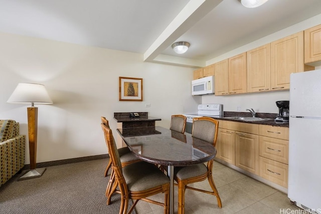 kitchen featuring dark countertops, baseboards, light brown cabinetry, white appliances, and a sink