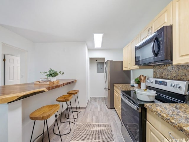 kitchen with a breakfast bar area, stainless steel appliances, light stone countertops, light hardwood / wood-style floors, and decorative backsplash