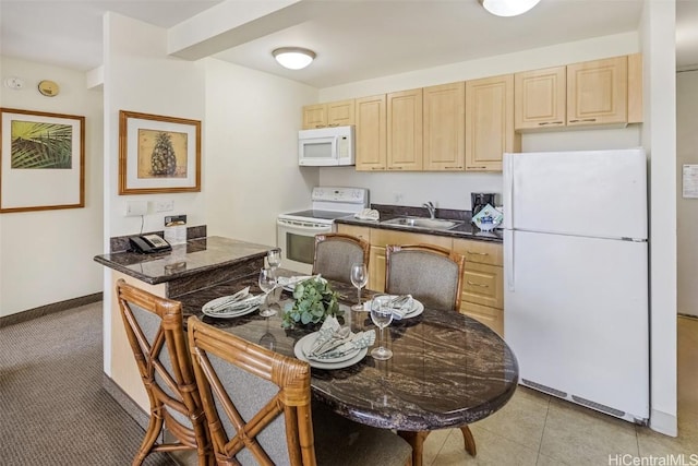 kitchen featuring light brown cabinets, white appliances, dark countertops, and a sink