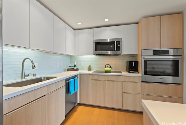 kitchen with sink, stainless steel appliances, light wood-type flooring, and tasteful backsplash