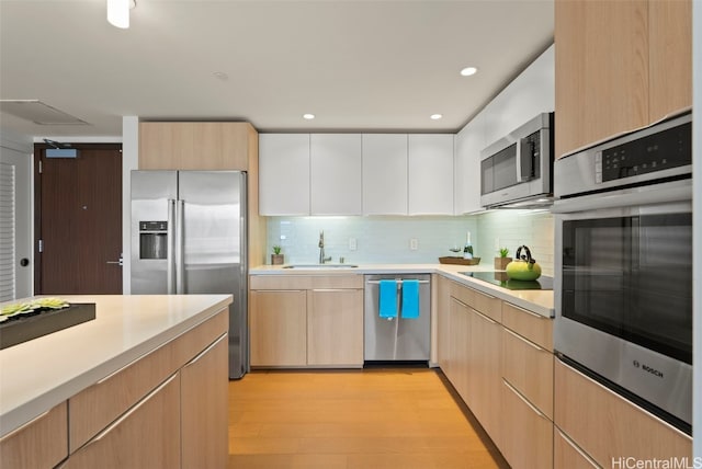 kitchen featuring appliances with stainless steel finishes, sink, backsplash, white cabinetry, and light hardwood / wood-style floors