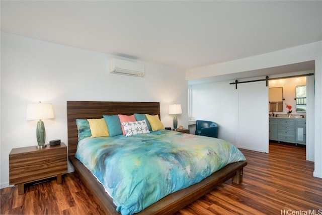 bedroom featuring connected bathroom, a barn door, dark hardwood / wood-style floors, and an AC wall unit