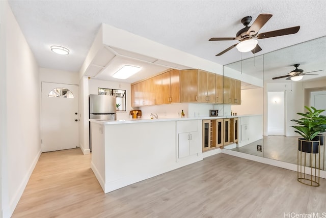 kitchen with kitchen peninsula, light hardwood / wood-style flooring, a textured ceiling, beverage cooler, and stainless steel refrigerator