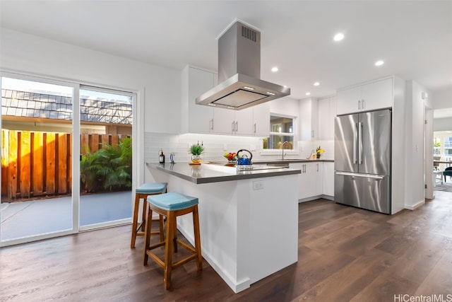 kitchen with a healthy amount of sunlight, stainless steel fridge, white cabinets, and island exhaust hood