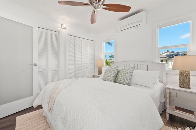 bedroom featuring two closets, dark hardwood / wood-style floors, a wall mounted AC, and ceiling fan