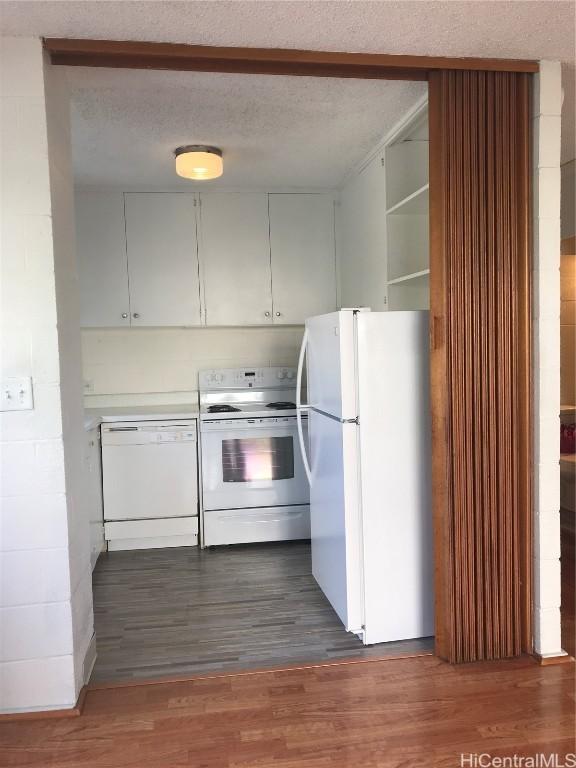 kitchen with dark wood-type flooring, white appliances, and a textured ceiling