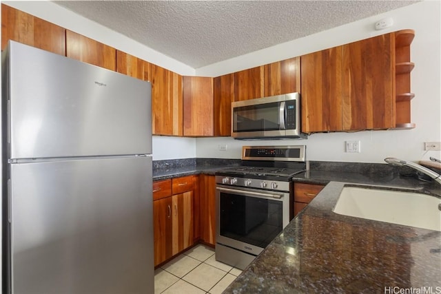 kitchen featuring sink, dark stone countertops, light tile patterned floors, stainless steel appliances, and a textured ceiling