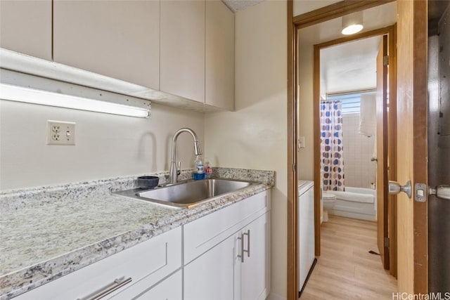 kitchen with white cabinetry, light stone counters, light wood-type flooring, and a sink